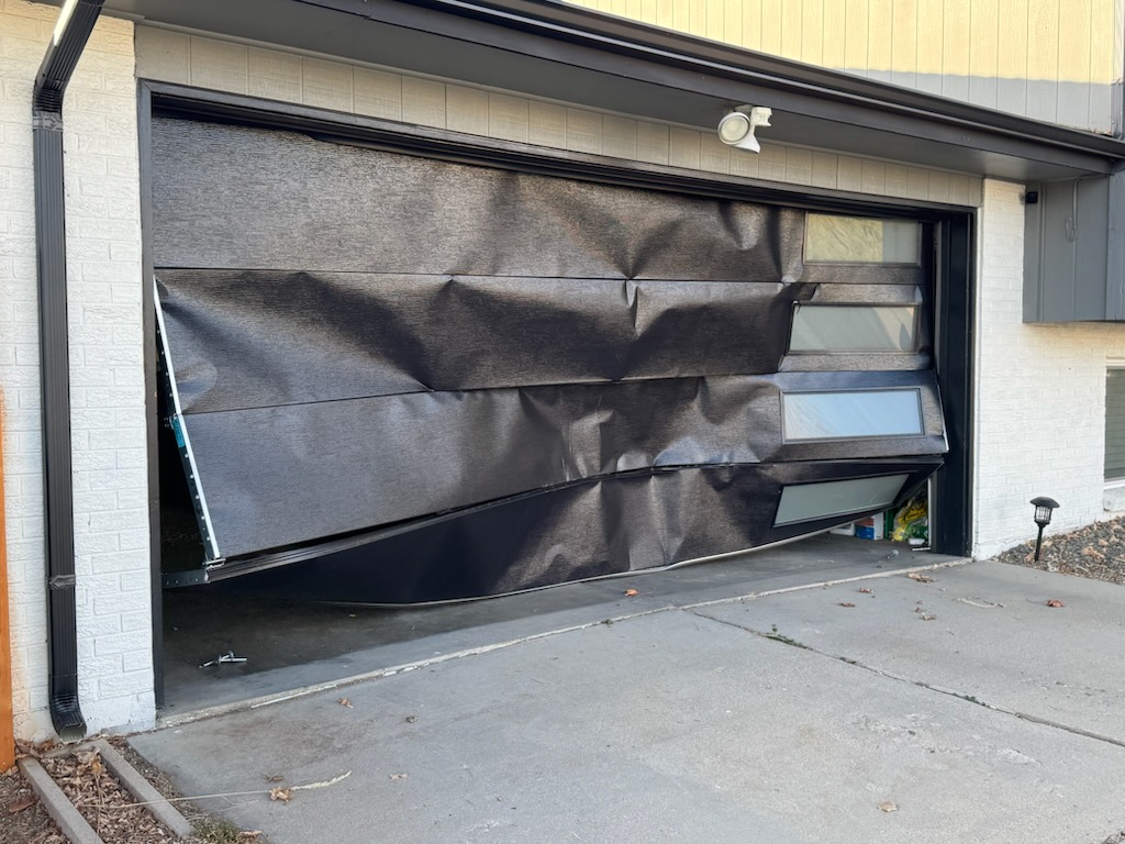 Damaged crumpled black garage door before replacement